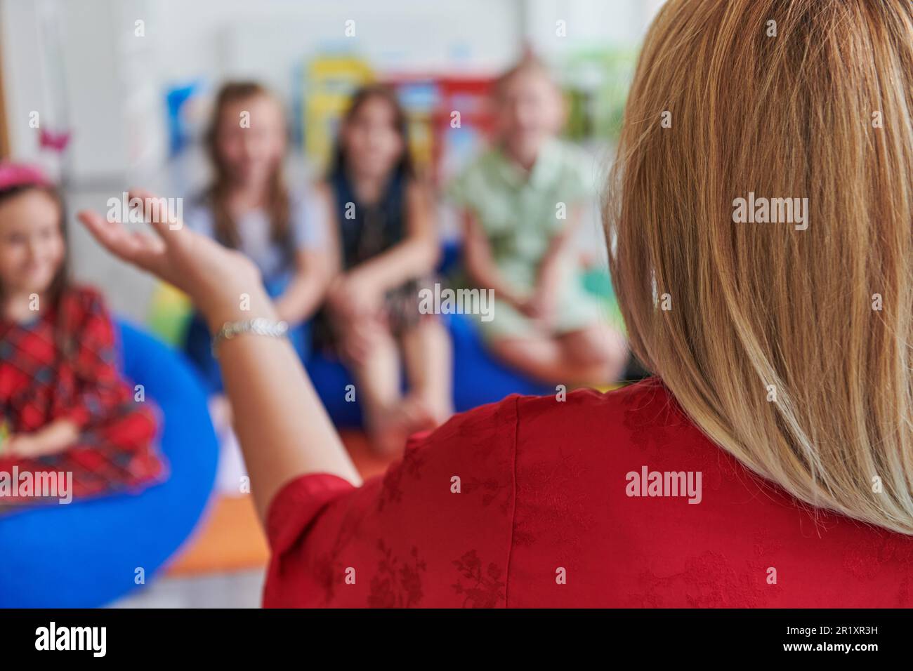 A happy female teacher sitting and playing hand games with a group of little schoolchildren