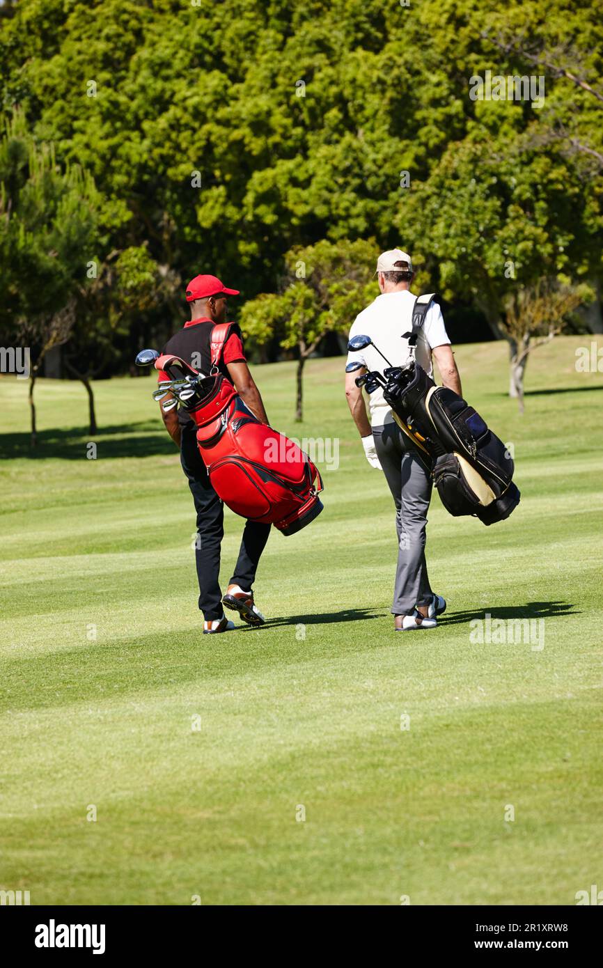 Trekking across the turf. two men carrying their golf bags across a golf course. Stock Photo