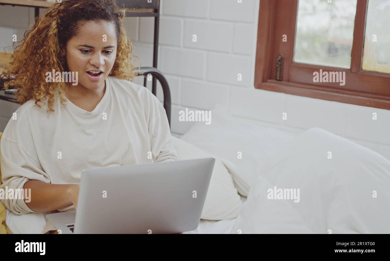 Young woman using laptop on bed at home in the morning. Stock Photo