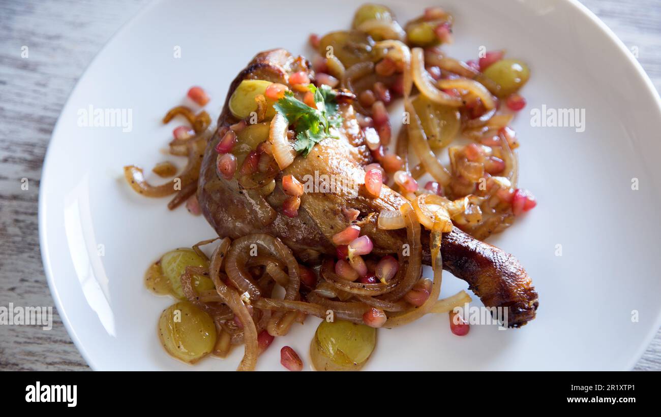 Duck confit with onion, pomegranate and grapes. Stock Photo