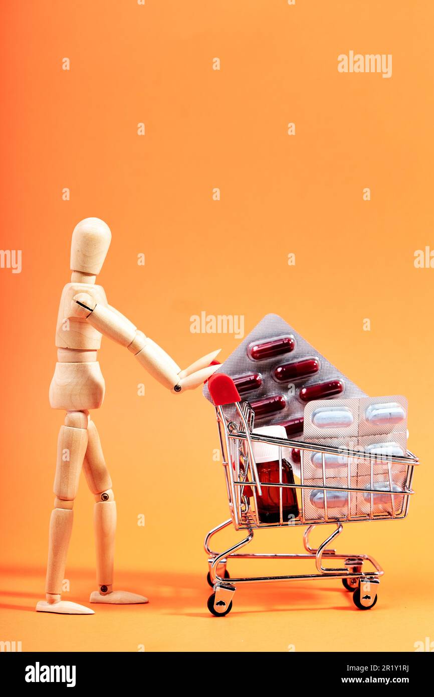 Dummy pushing a shopping trolley with medicines on an orange background. Health and medicine concept Stock Photo