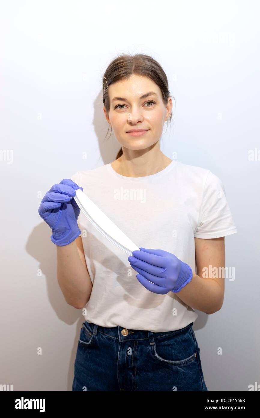 Caucasian manicurist, nail technician holds file in hands, wearing gloves. White smiling manicure master stands near gray wall in spa salon. Soft Stock Photo