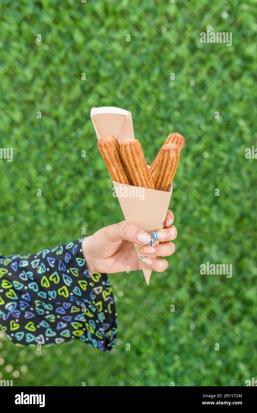 woman holding churros in cardboard box in front of green grass wall Stock Photo