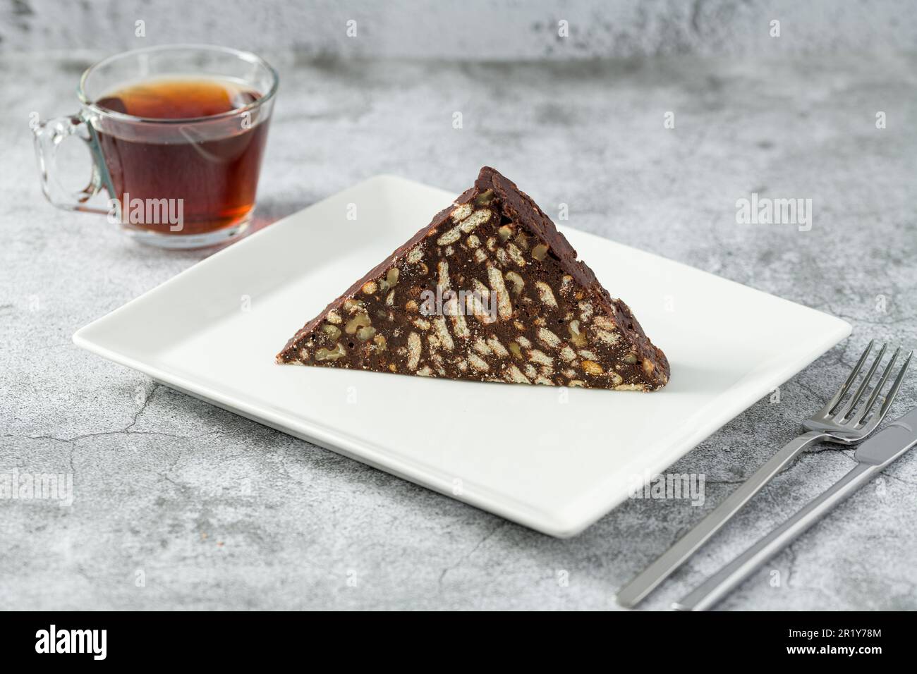 Chocolate mosaic cake with walnuts on a white porcelain plate on a stone background Stock Photo