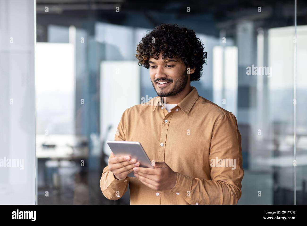 A smiling young Muslim man, businessman, student, designer standing in the office and using a tablet Stock Photo