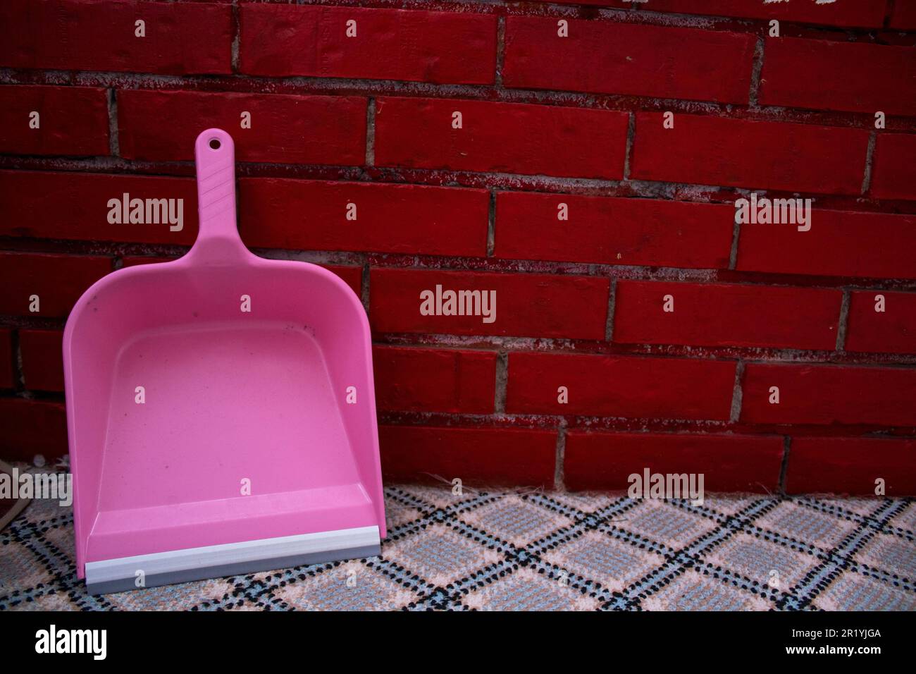 At home, leaning against the wall with a red brick pattern, pink, traditional shovel. Stock Photo