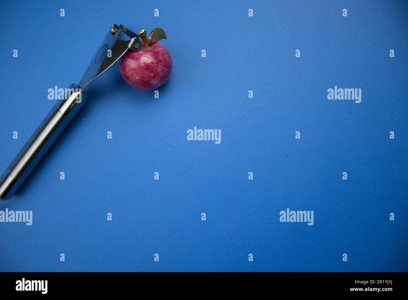 https://c8.alamy.com/comp/2R1YJYJ/placed-on-the-edge-of-the-blue-background-a-fruit-peeler-and-a-red-colored-stone-apple-2R1YJYJ.jpg