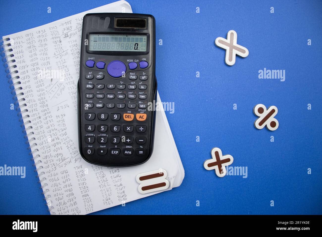 Placed on a blue background, a calculator, math signs and a notebook. Stock Photo