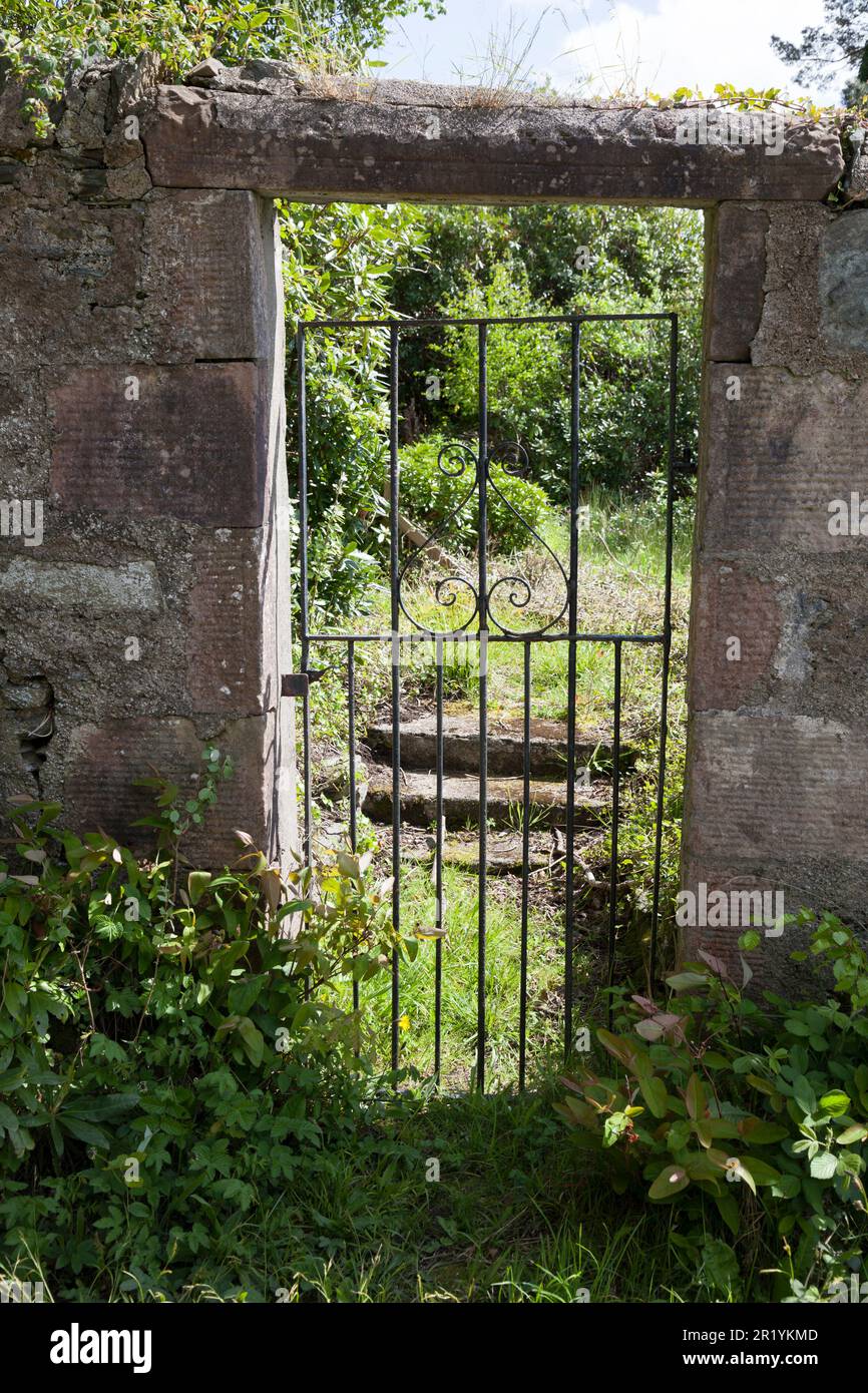 Old garden gate through stone wall, overgrown and crumbling Stock Photo
