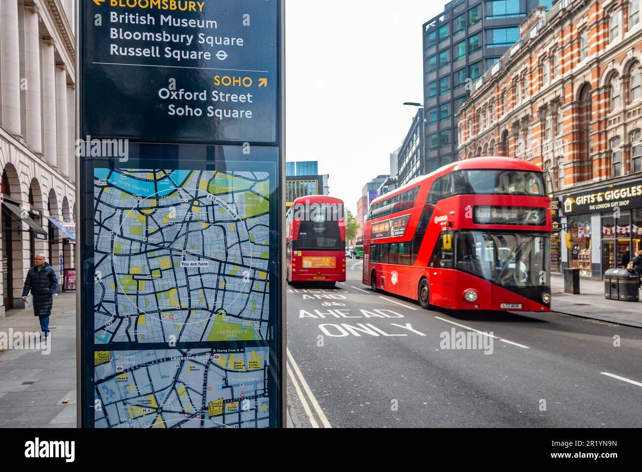 Iconic red London double decker buses seen on Tottenham Court Road. A sign with maps gives