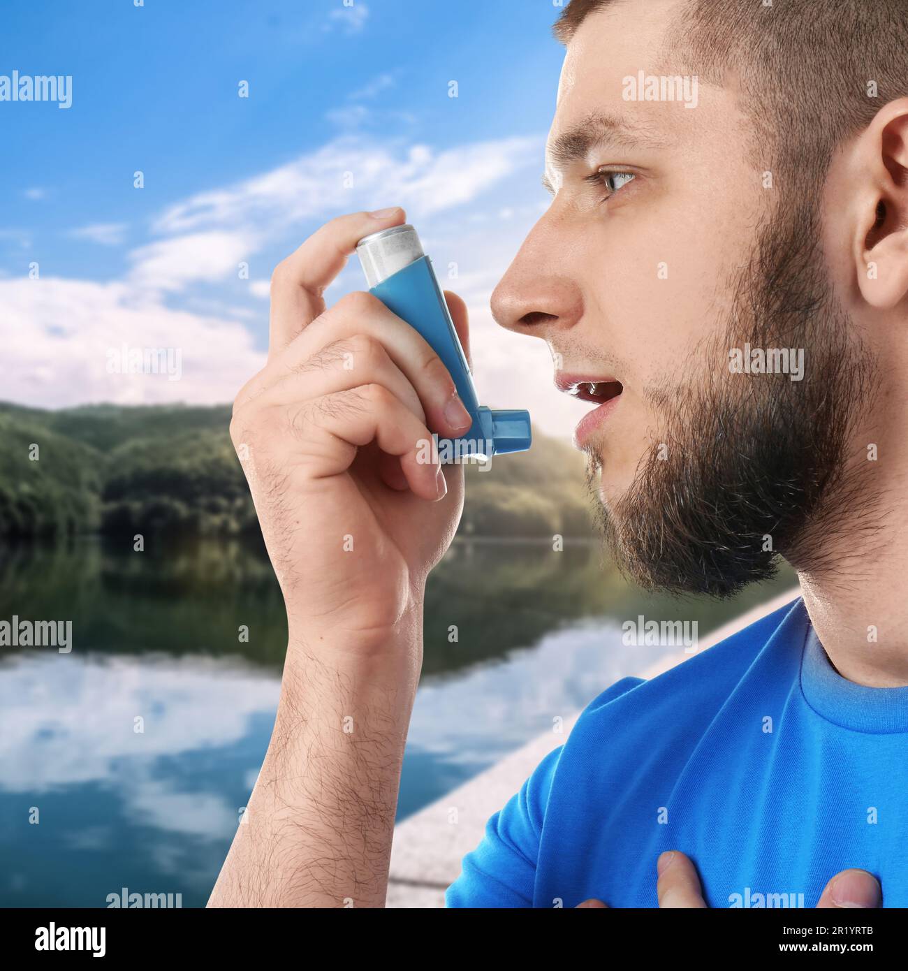 Man using asthma inhaler near lake. Emergency first aid during outdoor recreation Stock Photo