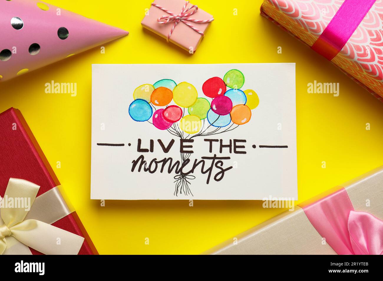 Life-affirming phrase Live The Moments. Flat lay composition with card and gift boxes on yellow background Stock Photo
