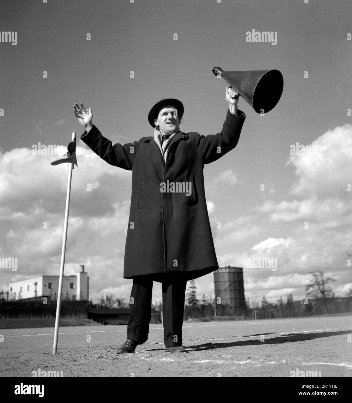 1940s man.  A man is standing on a football field cheering with raised arms with a megaphone in the left hand. Perhaps a lonely spectator at a football match. The megaphone was a device used to make your voice better and louder heard, screaming through it. 24 april 1949. Conard  ref 1104 Stock Photo