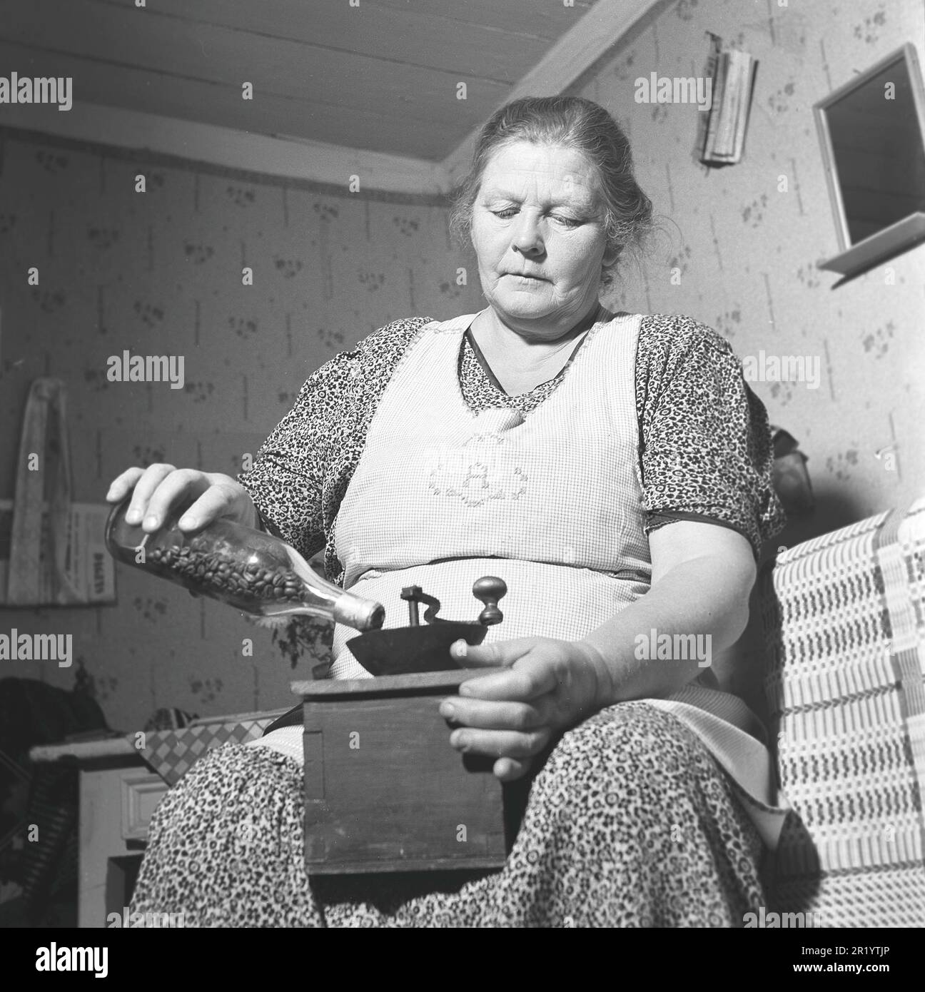 Grinding coffee in the 1940s. Mrs. Anna Karlsten grinds coffee beans manually in a coffee grinder. Coffee was at this time during the time of world war II very scarse and expensive, and rationed. She stores them in a glass bottle and pours them in to start. Sweden 1942. Kristoffersson ref 226-17 Stock Photo