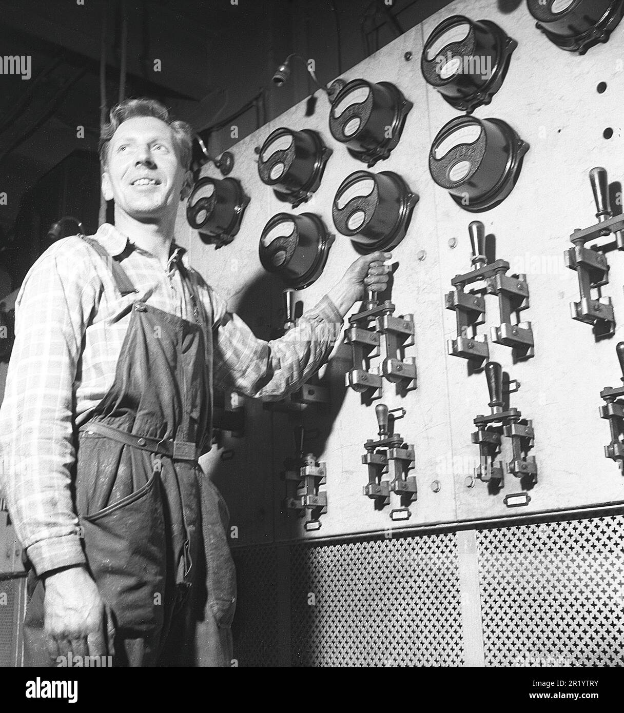 Man and machine in the old days. A man stands in front of a wall filled ...