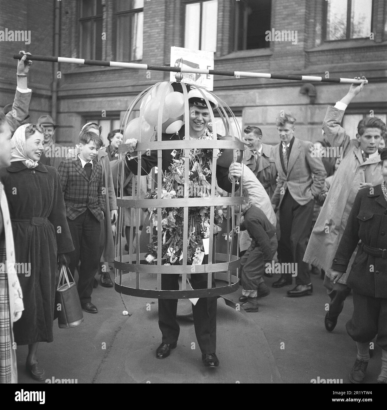 In the 1950s. The graduation day when finishing exams and leaving school is usually a festive day with family and friends celebrating the students achievements both pranking him with costumes and giving gifts and flowers. This young man is put in a cage and paraded in the street. Sweden 1953 Kristoffersson ref BL79-1 Stock Photo