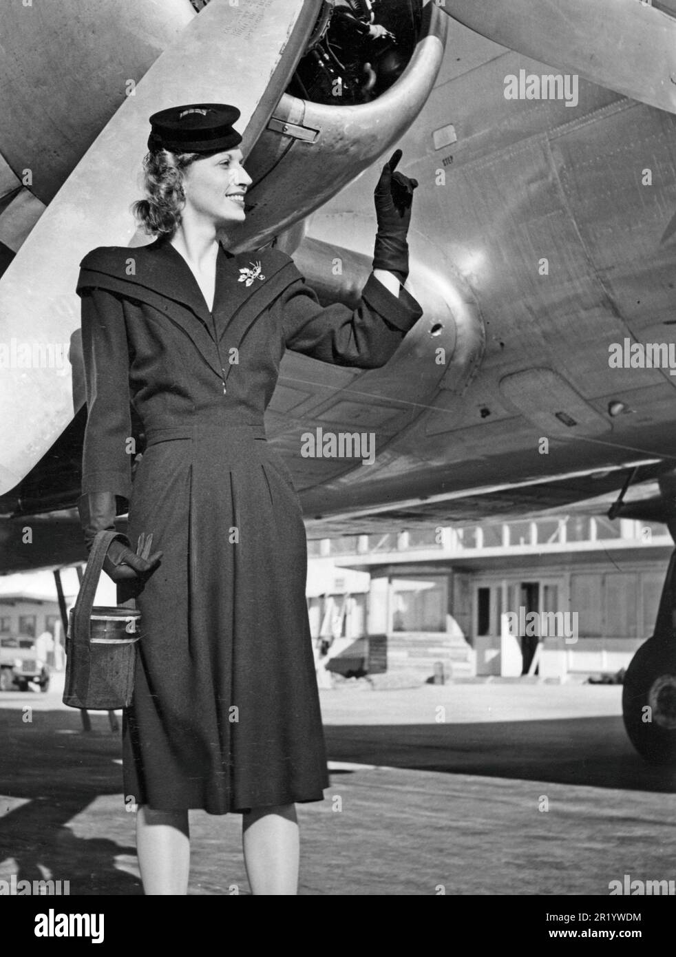 Women's fashion in the 1940s. A young woman on Bromma airport stands outside the plane. She is fashionably dressed in a dark outfit, matching hat, dark gloves and a round purse. Sweden 1944. Stock Photo