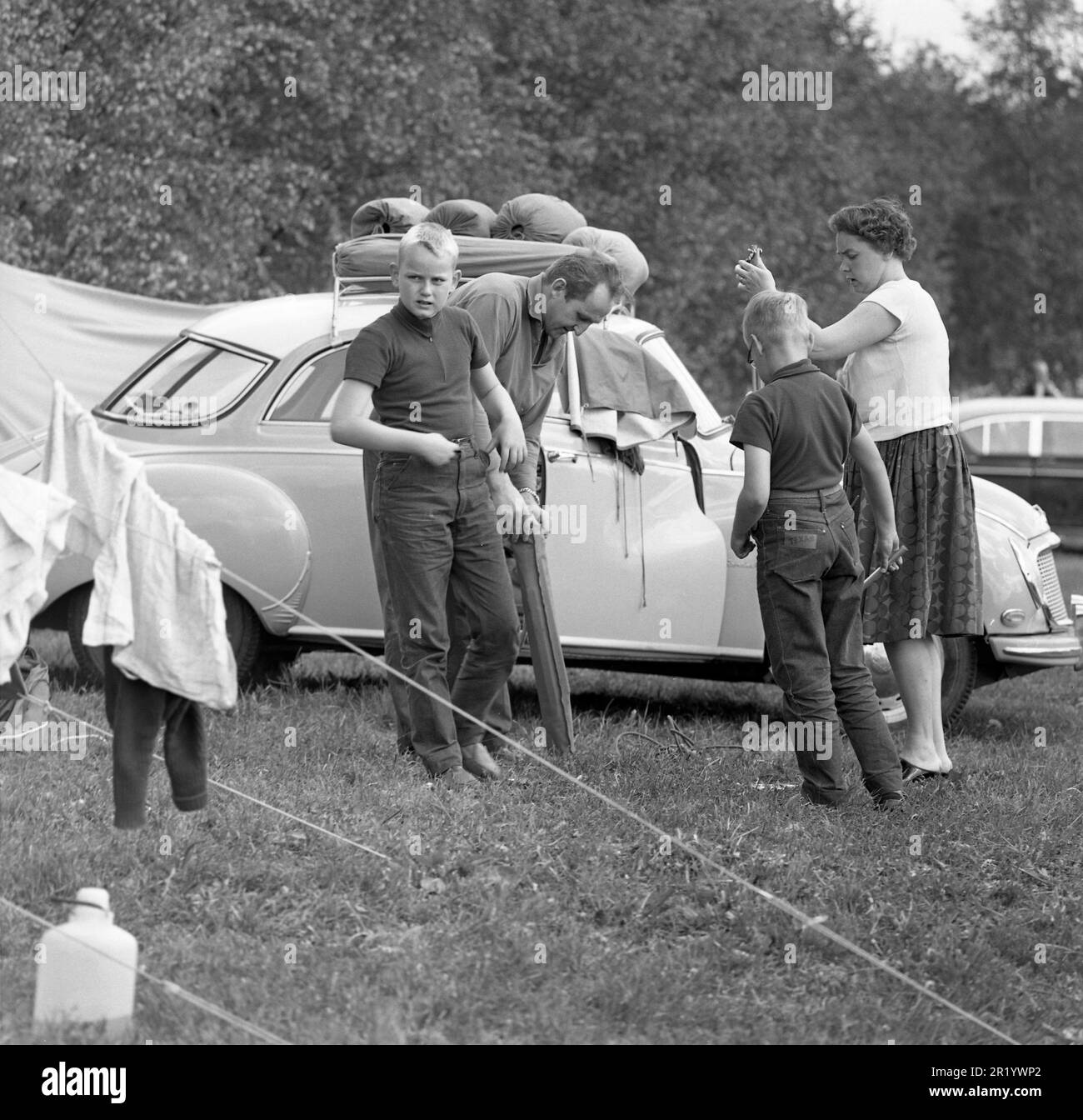 Camping in the 1960s. A campsite where this family spend parts of their summer holiday.  Their car is seen in the background with the camping gear transported on the roof rack. Värmland Sweden 1962. ref BV99-7 Stock Photo