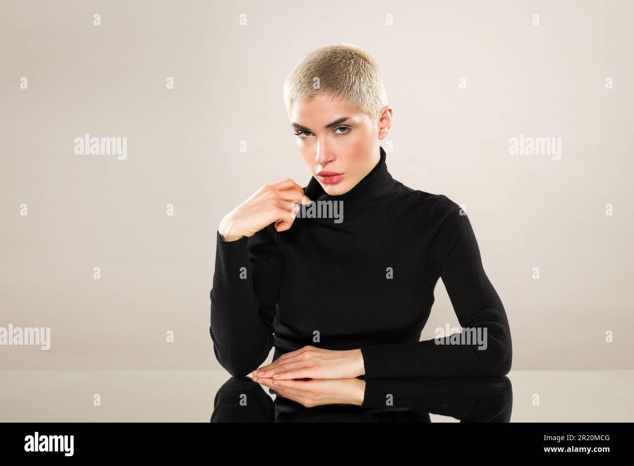 Portrait of serious young female in black turtleneck with short blond hair looking at camera against beige background Stock Photo