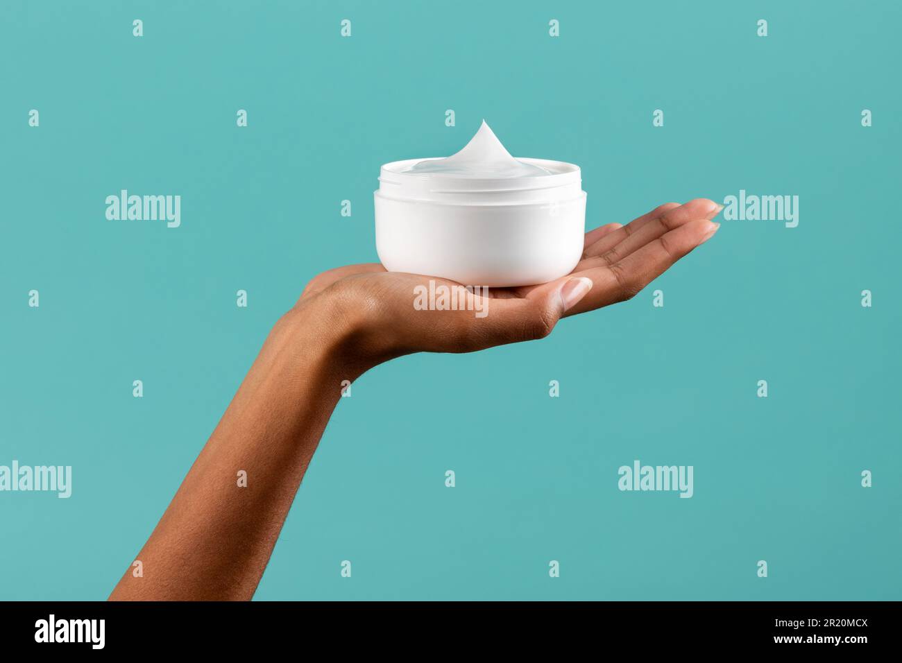 Unrecognizable African American female showing white plastic jar with body cream against turquoise background Stock Photo