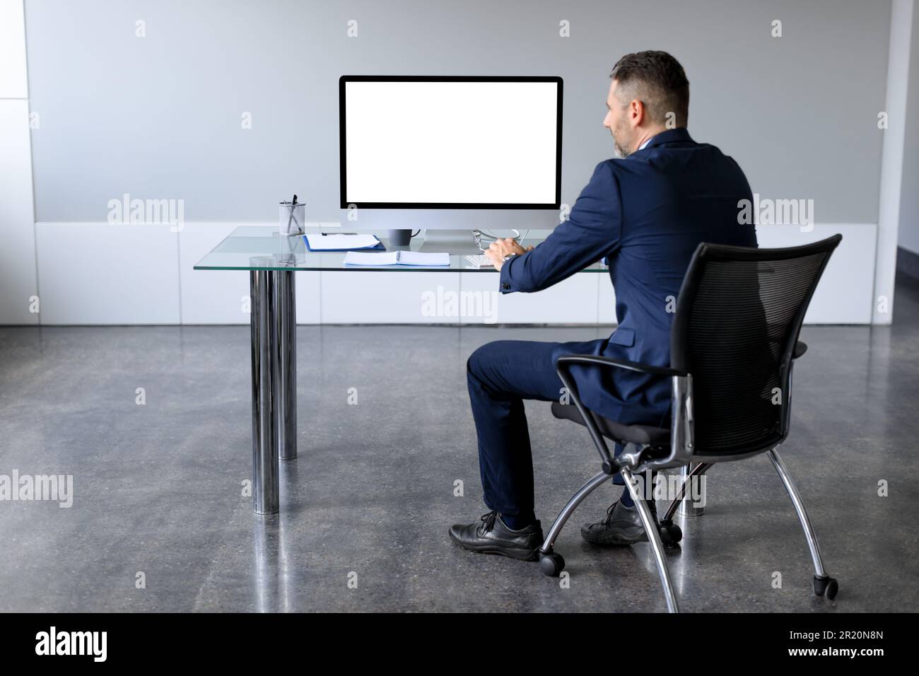 Rear back view of businessman in suit looking at pc computer with blank screen for mock up, sitting at desk in office Stock Photo