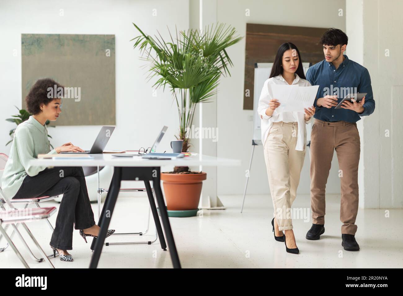 Three Business Professionals Working Using Computers, Reading Papers In Office Stock Photo