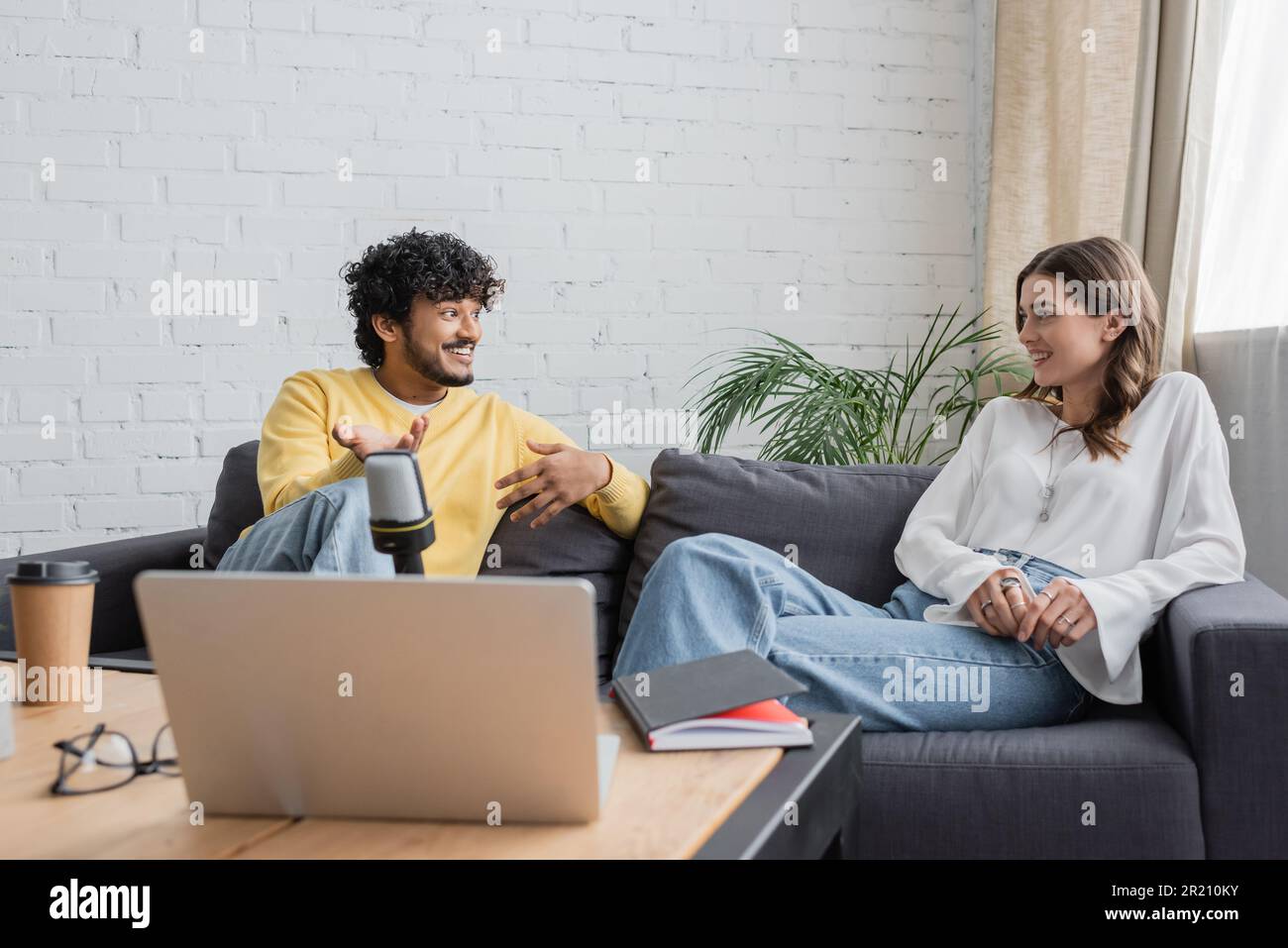 young indian man in yellow jumper and smiling brunette woman sitting on ...