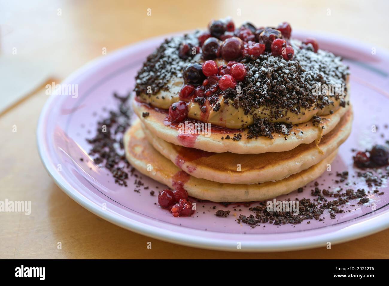 Stacked pancakes with peanut butter cream, berries, crumble and icing sugar on a plate, sweet breakfast, brunch or dessert dish, selected focus, narro Stock Photo