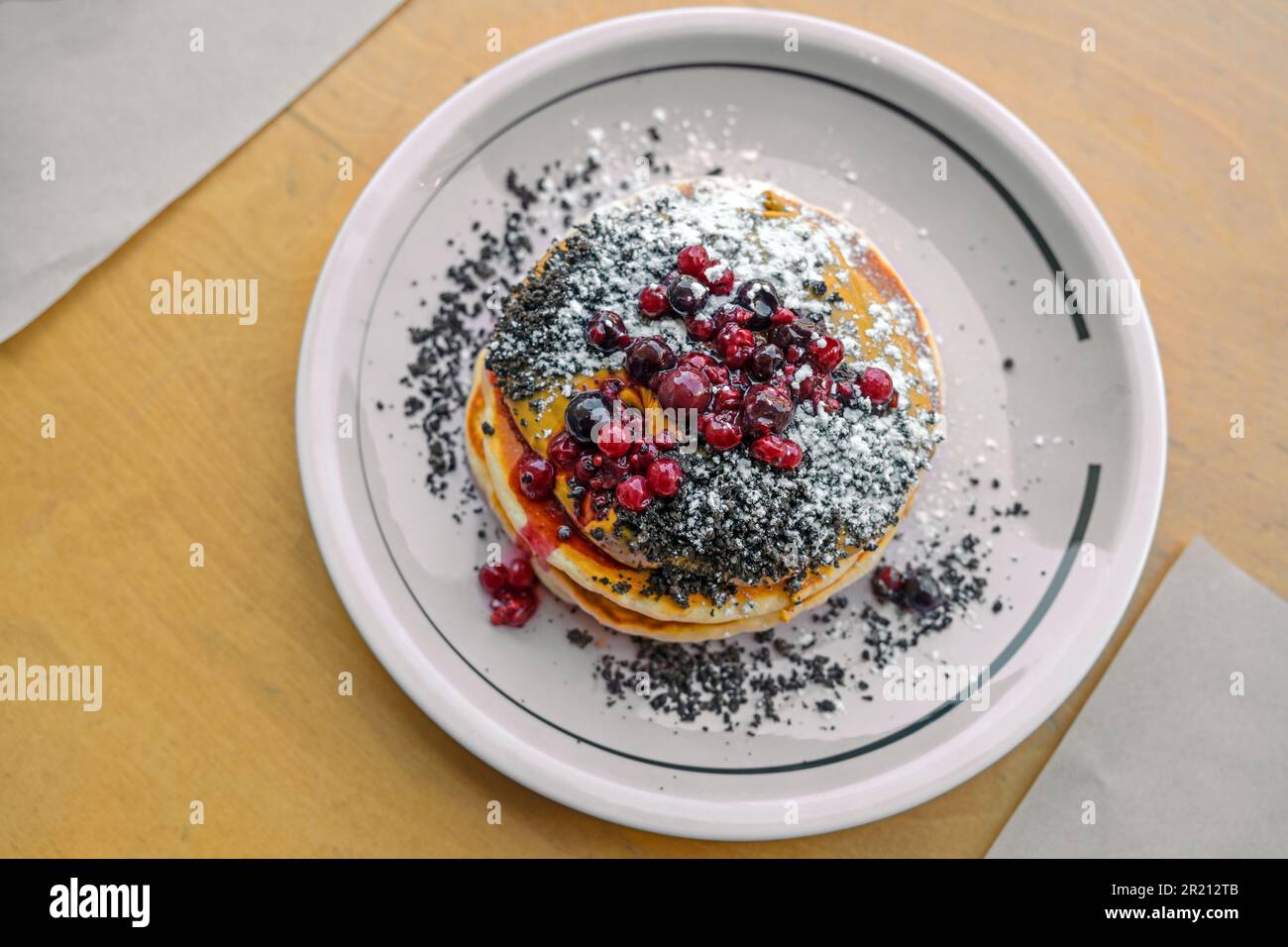 Pancakes with peanut butter cream, berries, crumble and icing sugar on a plate and a wooden table, sweet brunch or dessert dish, top view from above, Stock Photo