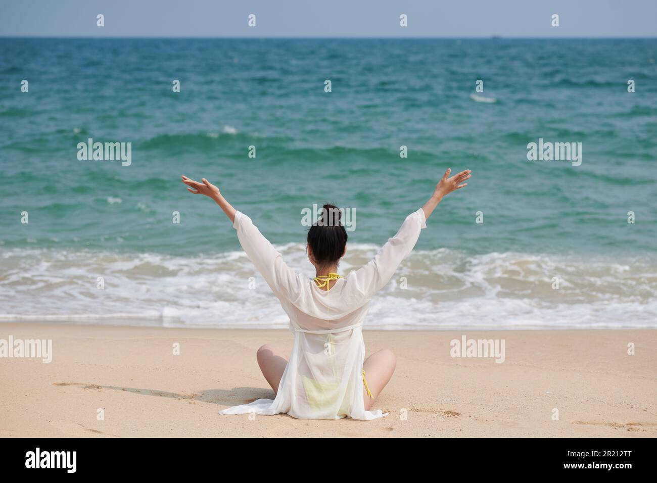 Young woman sitting on sea beach enjoying sound of waves Stock Photo