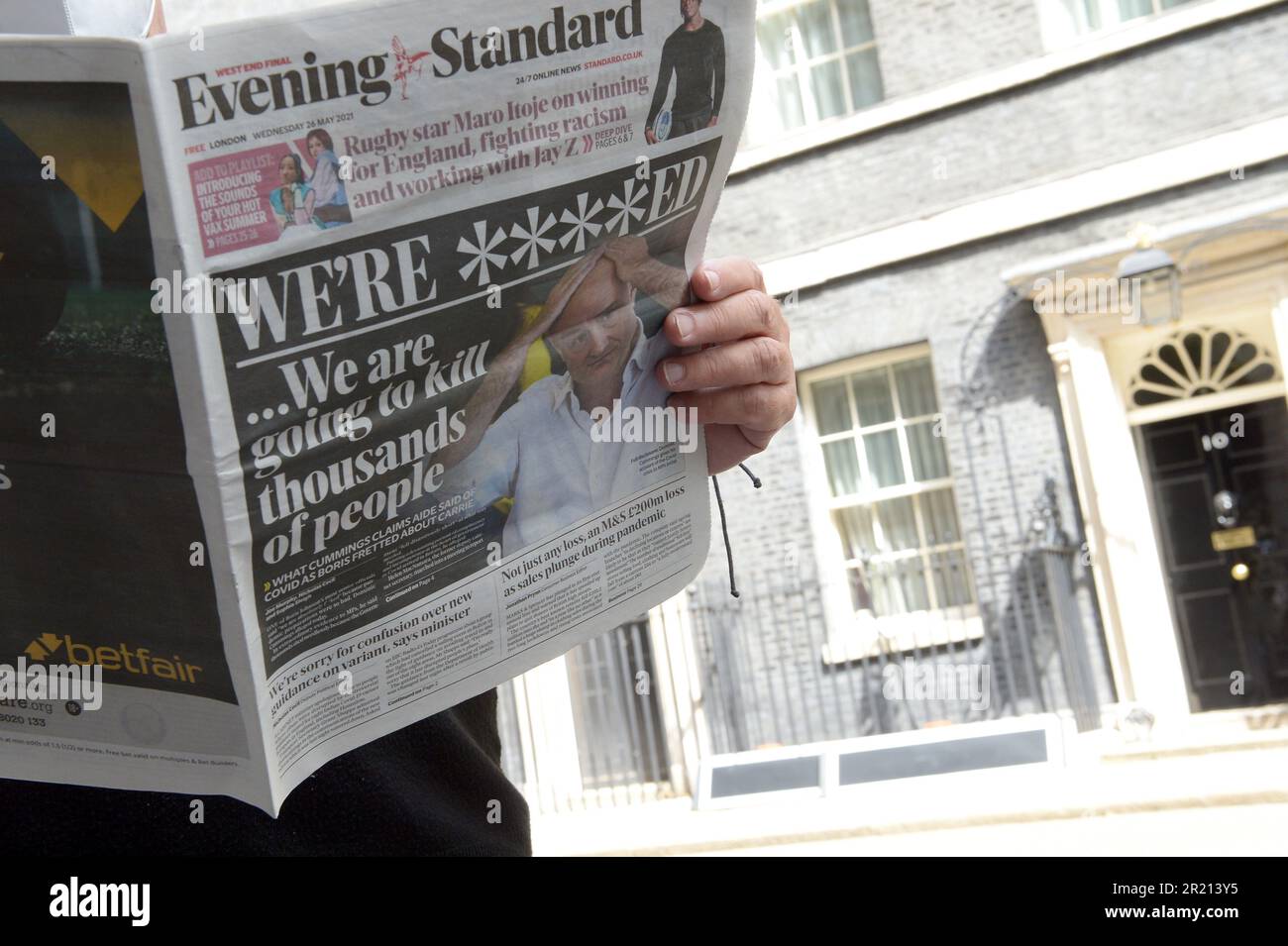 A man stands in Downing Street holding a copy of the Evening Standard dated 26th May 2021 which leads with Dominic Cummings testimony to the Select Committee in which he said that Boris Johnson treated COVID-19 like a 'scare story' and that health secretary Matt Hancock should have been 'sacked for lying' whilst saying that pandemic preparations were so bad that he exclaimed 'we are f***ed... we are going to kill thousands of people' Stock Photo