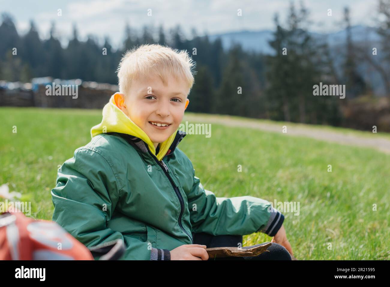Fun teenager sits on hillside. Boy resting in mountains. School boy