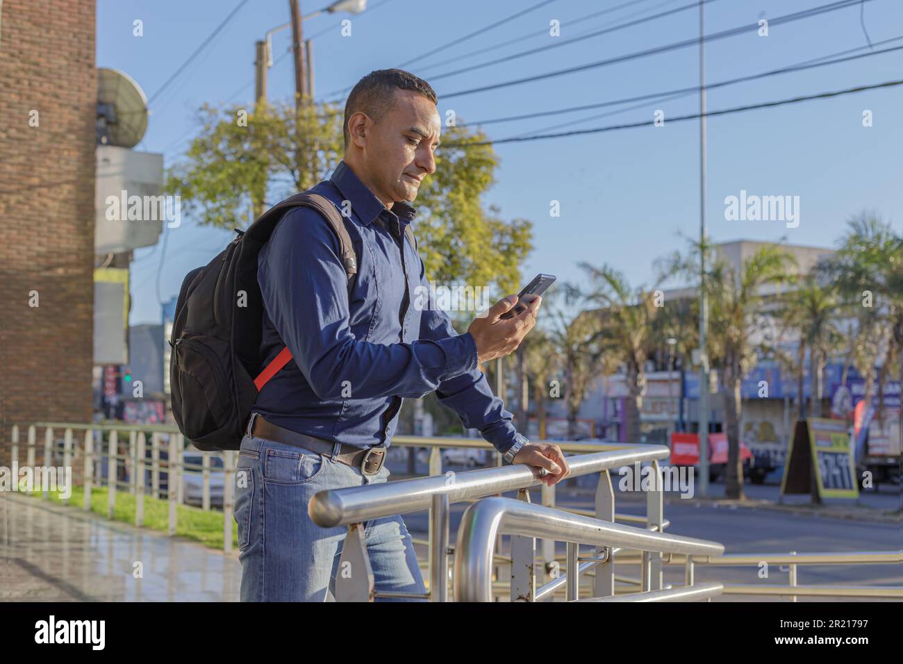 Young latin man with backpack looking at his mobile phone. Stock Photo