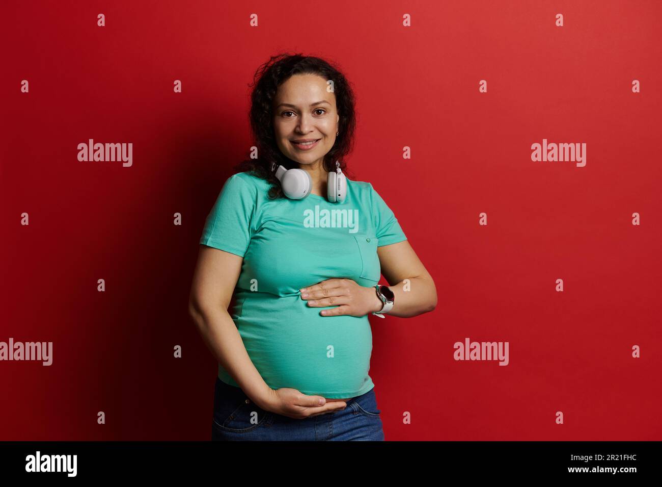 Beautiful pregnant woman with hands on her belly, feeling happy by