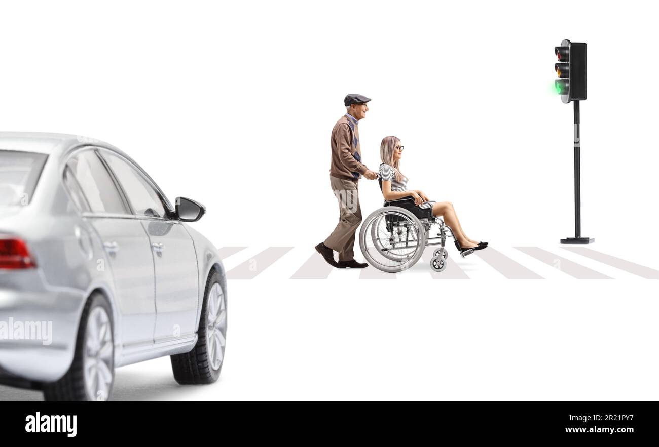 Elderly man pushing a young woman in a wheelchair at a pedestrian crossing isolated on white background Stock Photo