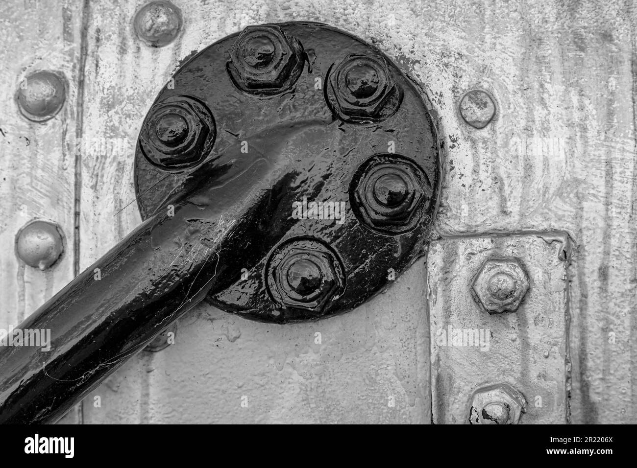 A grayscale closeup of an industrial metal tube with large bolts