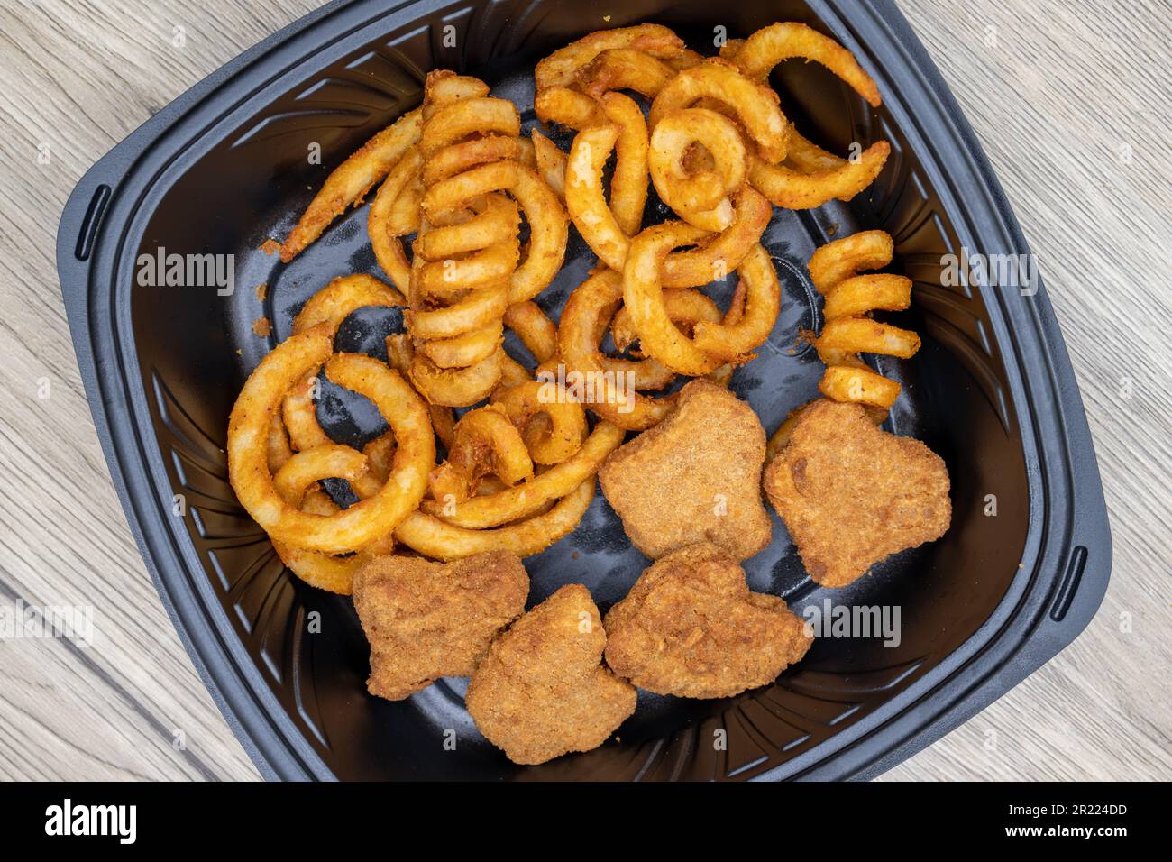 Overhead view of to go order of curly french fries and chicken nuggets are packed in plastic container with dressing on the side. Stock Photo