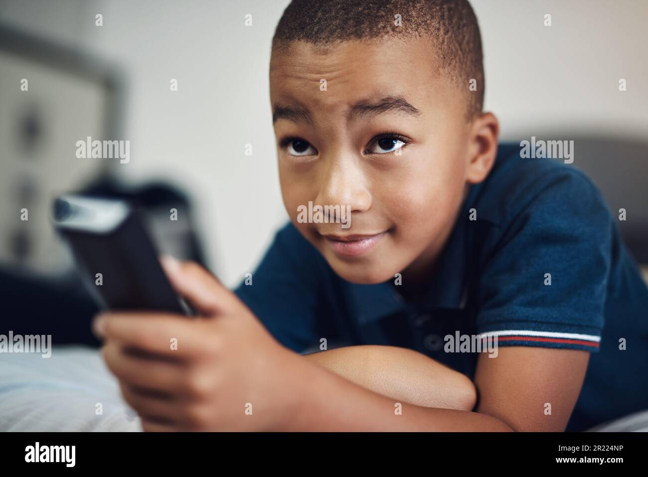 When exposed to the right shows, your child can learn useful things. a young boy using a remote control while lying on his bed. Stock Photo