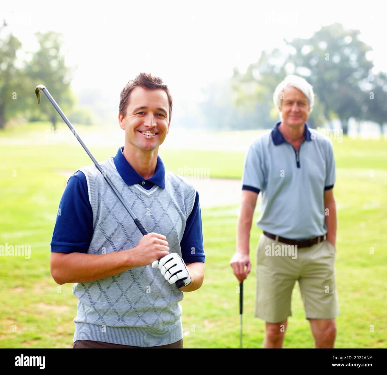 Smart golfer smiling. Portrait of smart man holding a golf club and smiling with father standing in background. Stock Photo