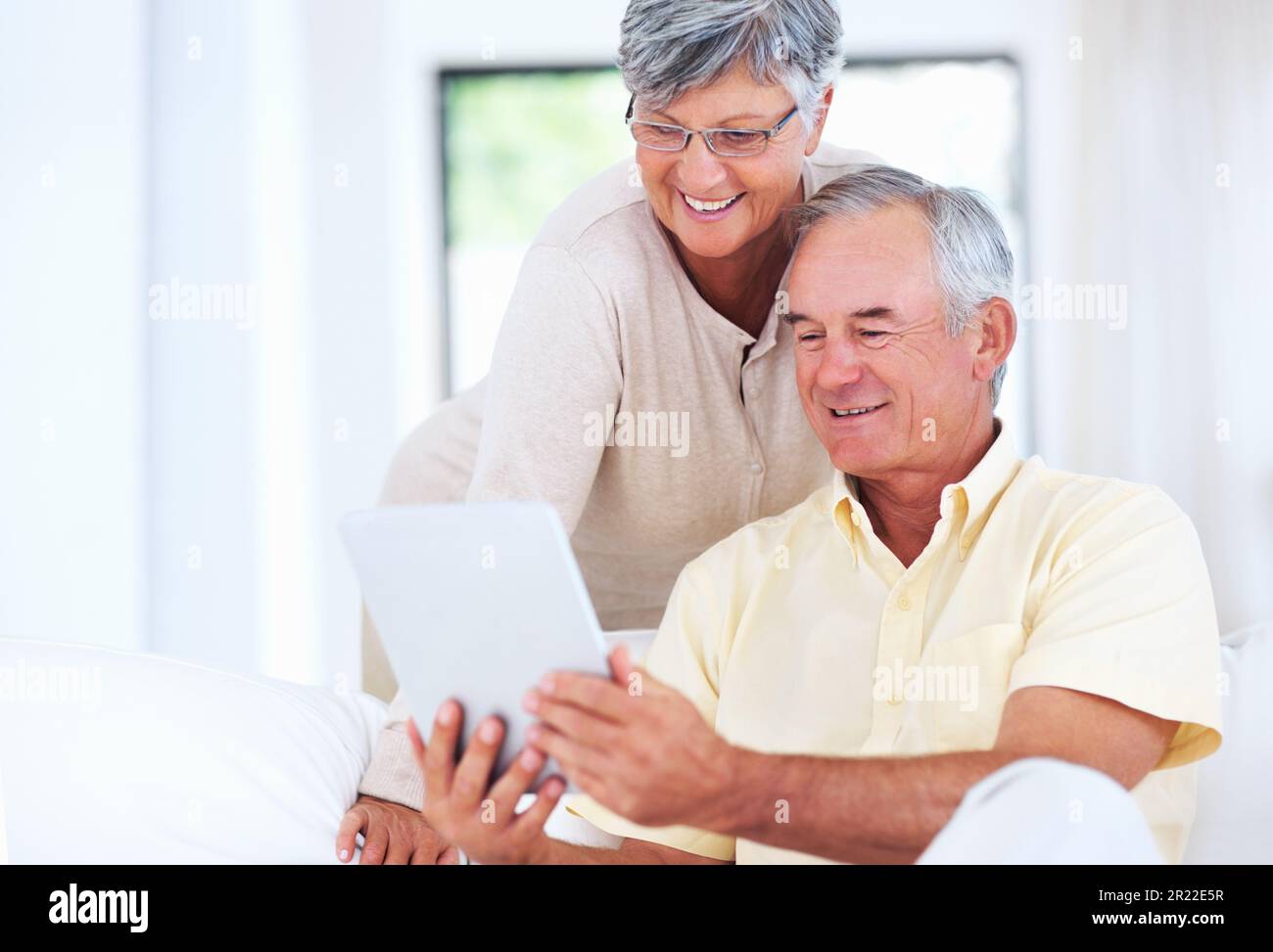 Couple using digital tablet at home. Cheerful mature couple smiling while using digital tablet at home. Stock Photo