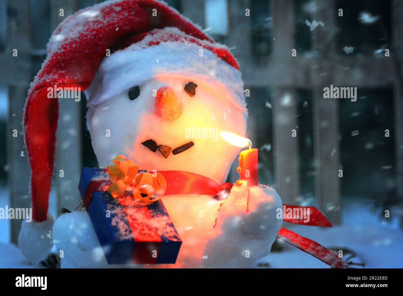 snow man with Santa Claus cap, burning candle in its hand and Christmas gift Stock Photo