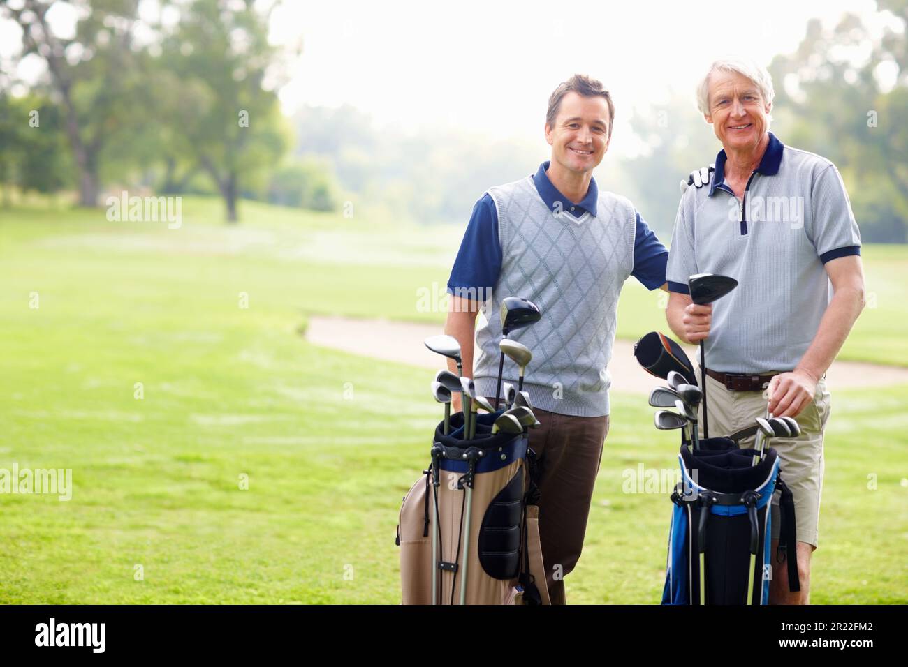 Father and son smiling on golf course. Portrait of father and son standing with golf bags and smiling. Stock Photo