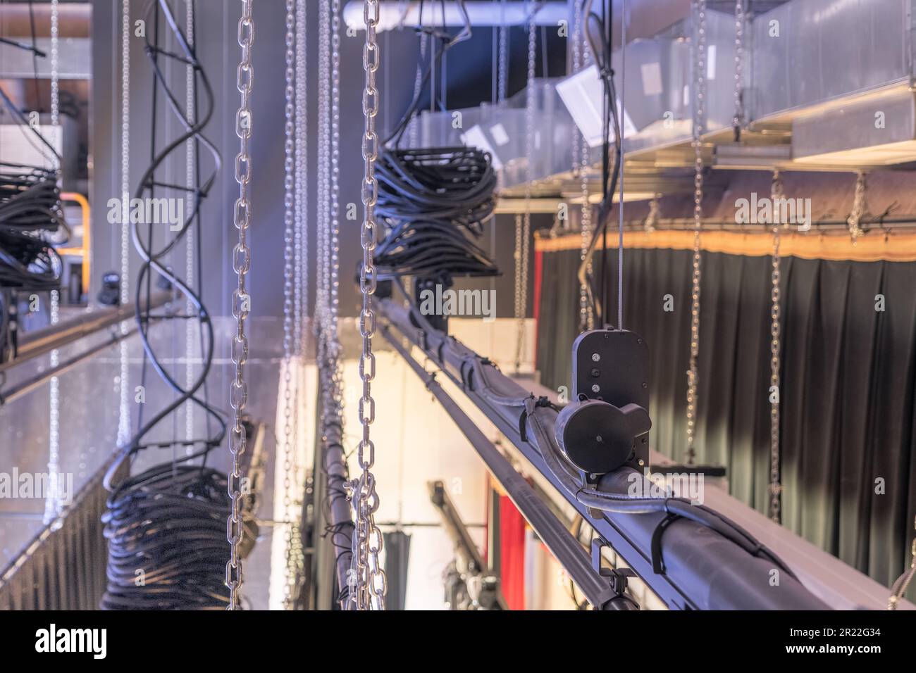 Theater stage rigging with theatrical equipment, lighting, supports, and chains.  Photo taken from an elevated position looking across the rigging. Stock Photo