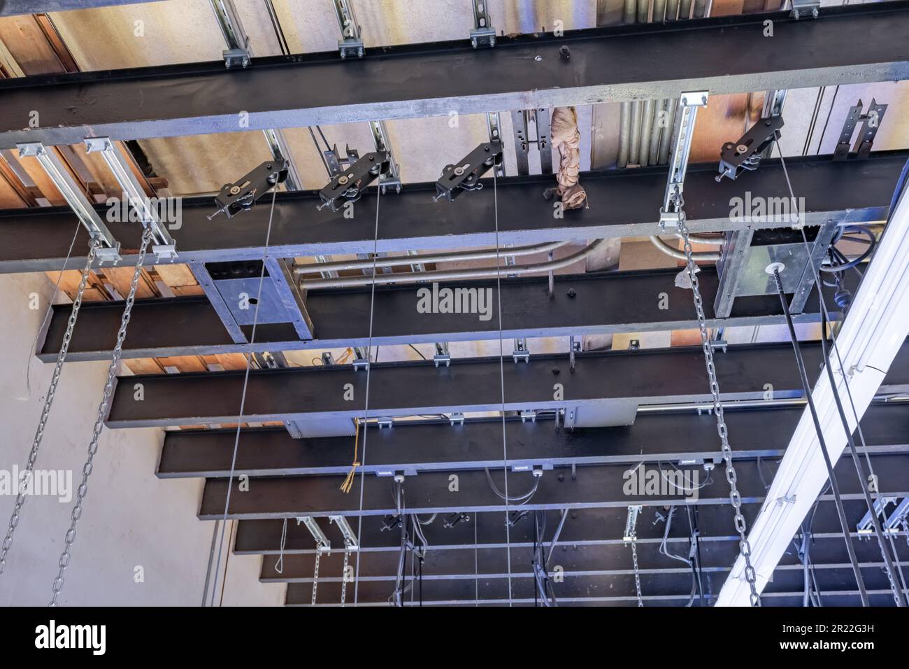 Theater stage rigging with theatrical equipment, lighting, supports, and chains.  Photo taken from an elevated position looking across the rigging. Stock Photo