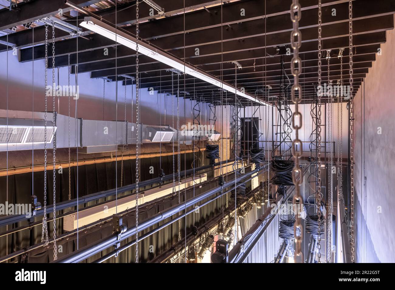 Theater stage rigging with theatrical equipment, lighting, supports, and chains.  Photo taken from an elevated position looking across the rigging. Stock Photo