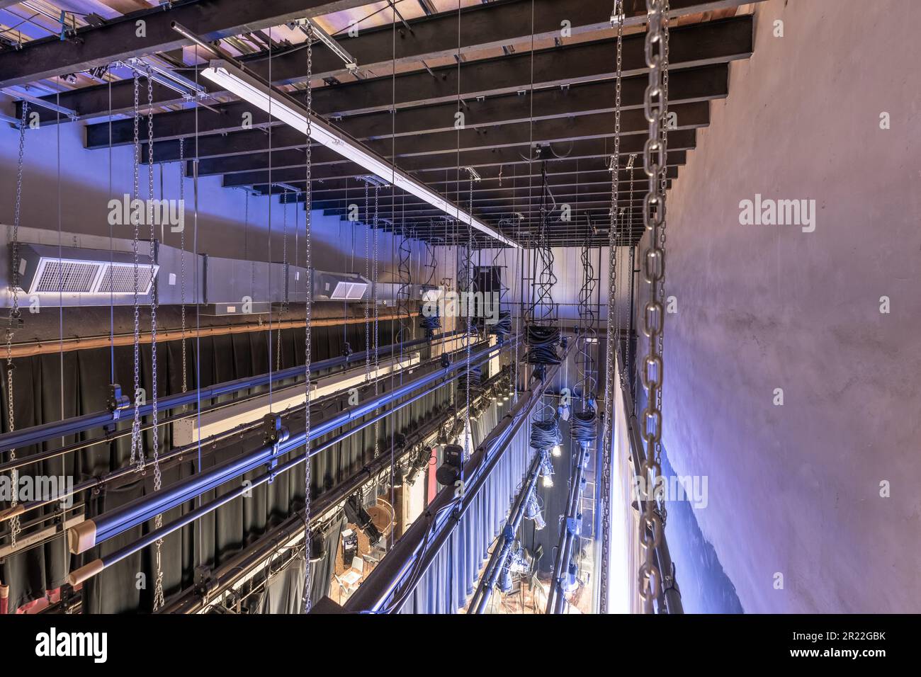 Theater stage rigging with theatrical equipment, lighting, supports, and chains.  Photo taken from an elevated position looking across the rigging. Stock Photo