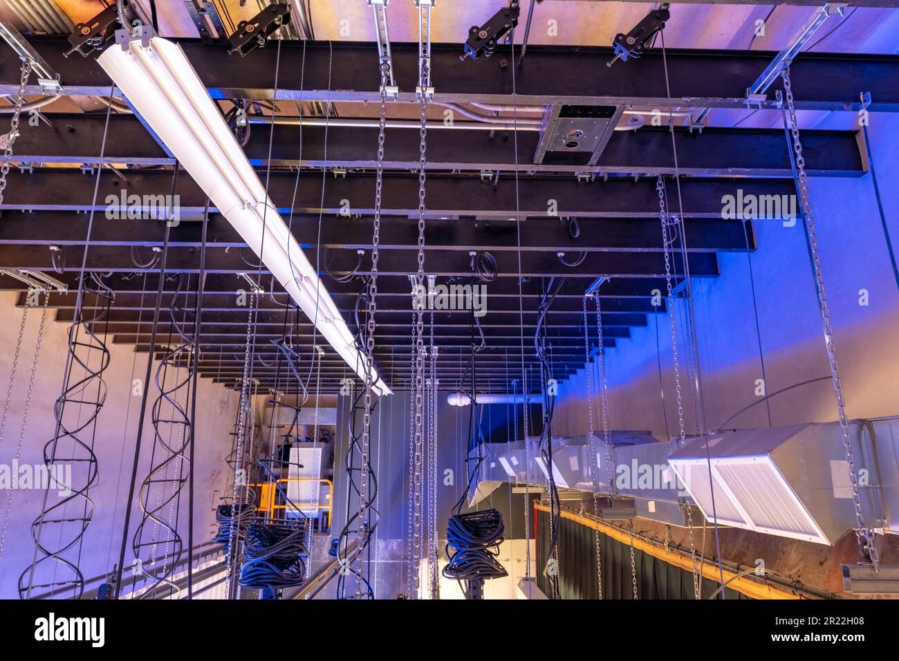 Theater stage rigging with theatrical equipment, lighting, supports, and chains.  Photo taken from an elevated position looking across the rigging. Stock Photo