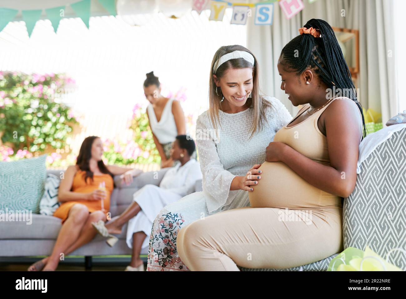 This feels so wonderful. a young woman feeling her friends baby move in her belly during her baby shower. Stock Photo