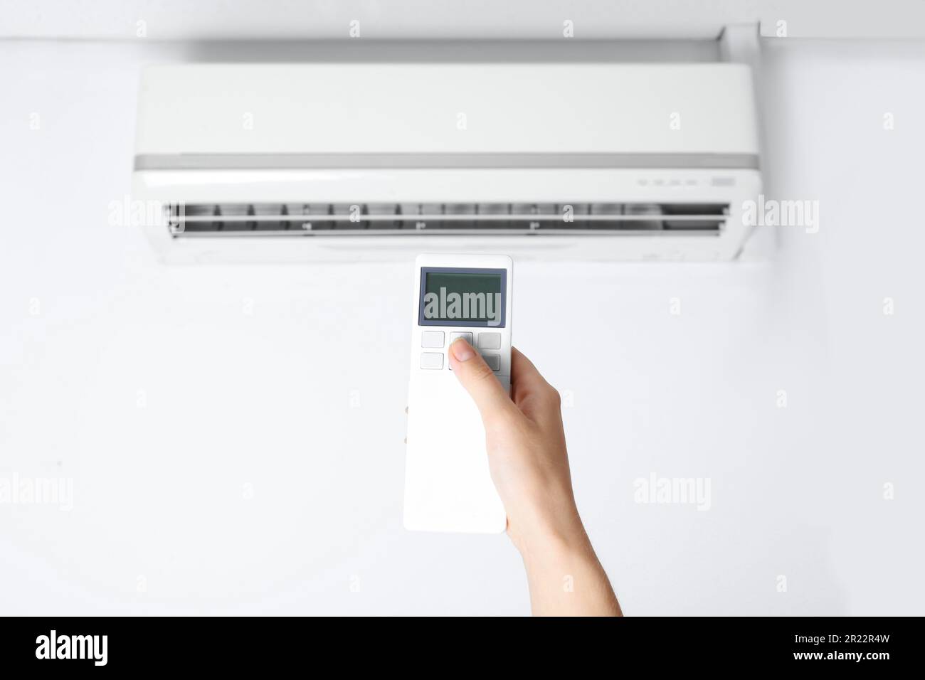 Woman operating air conditioner with remote control indoors, closeup ...