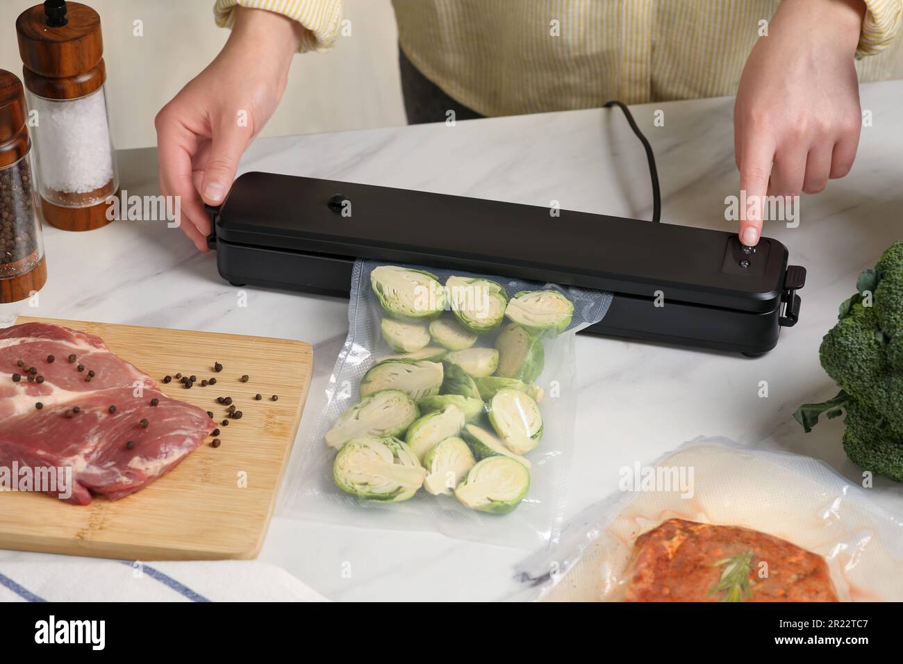 Woman using sealer for vacuum packing with plastic bag of zucchini at
